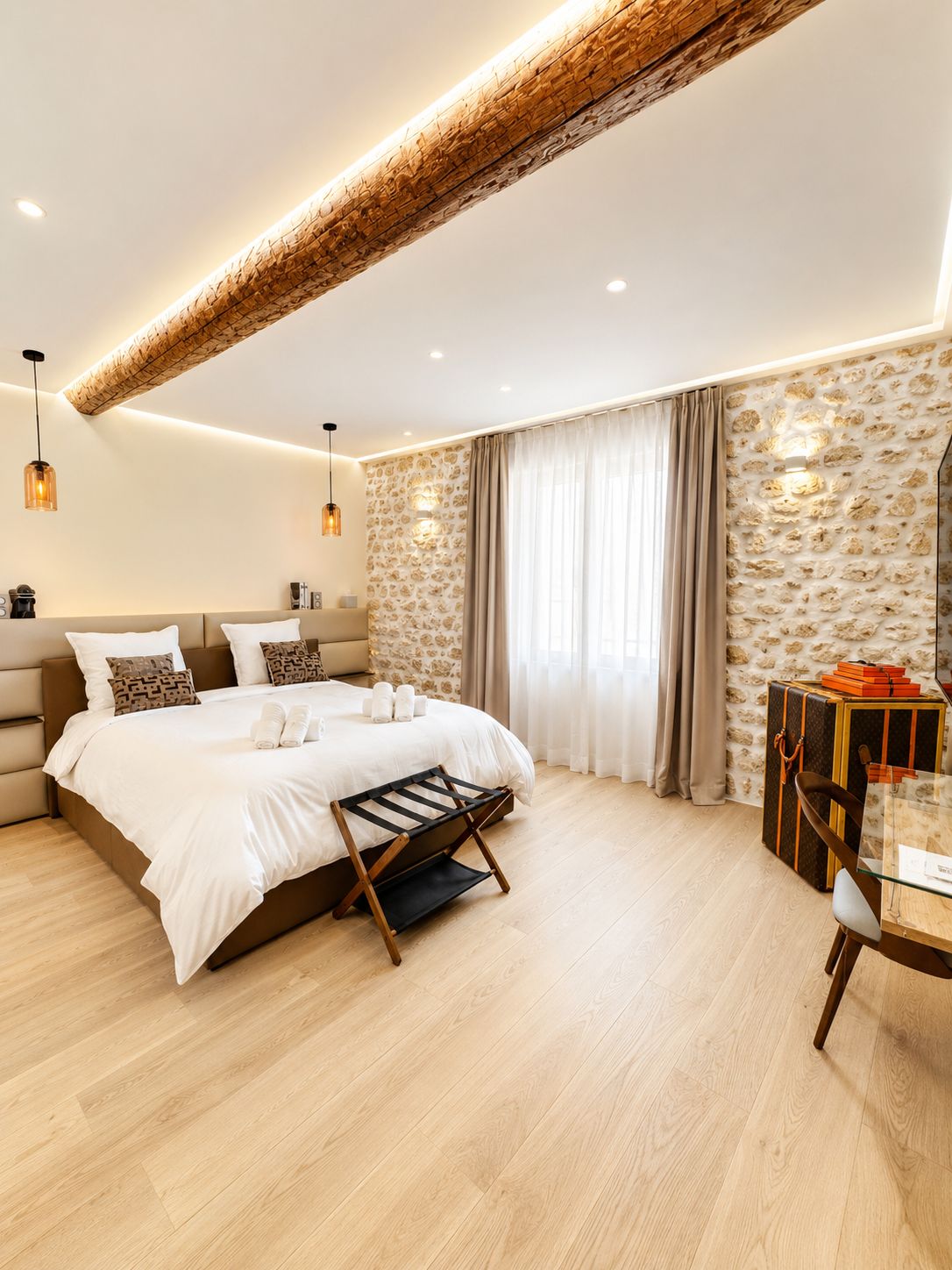 A modern bedroom with a large bed, a wooden ceiling, and a stone wall.