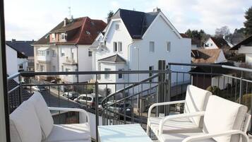 Ein Balkon mit weißer Gartenmöbeln, einem Metallgeländer und Blick auf Wohnhäuser im Hintergrund.