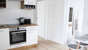 Eine moderne Küche mit weißen Schränken, einem Einbauofen und einer Kaffeemaschine. Es gibt einen Essbereich mit einem weißen Tisch und Stühlen.