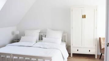 Ein Schlafzimmer mit einem weißen Bett, einem weißen Kleiderschrank und Holzboden.