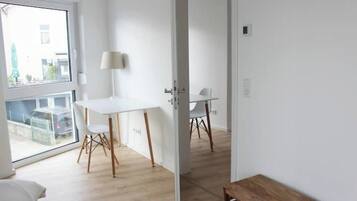 Ein modernes Zimmer mit großem Fenster, einem weißen Tisch mit Stühlen und einer hölzernen Bank.
