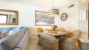 A living room with a sofa, wicker chairs, a round table with a bowl, a wall clock, and a framed artwork. - Phoenix East 2 2074 2 Bedroom Condo (Orange Beach)