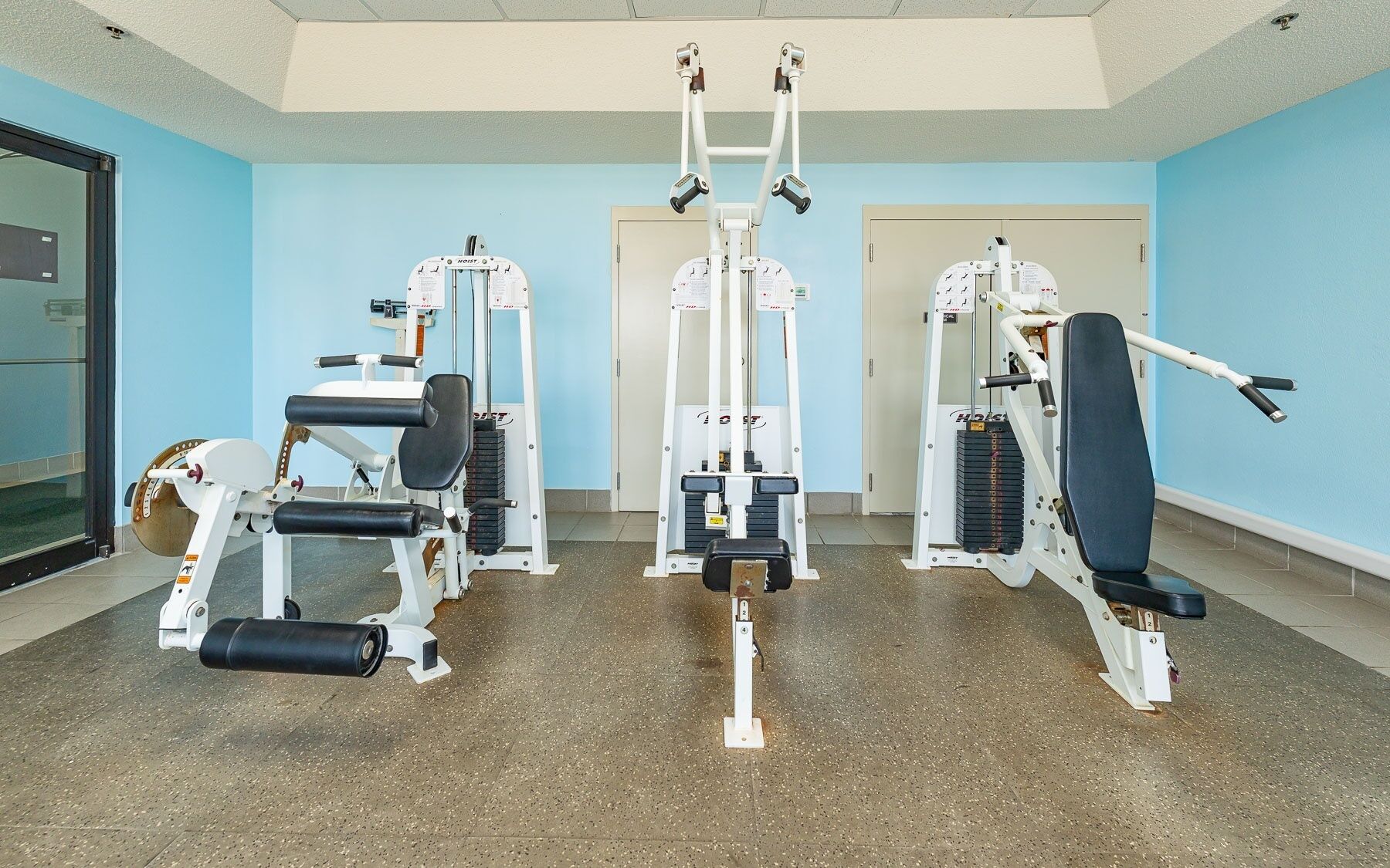 Un gimnasio con diferentes máquinas de ejercicio, una puerta y una ventana.