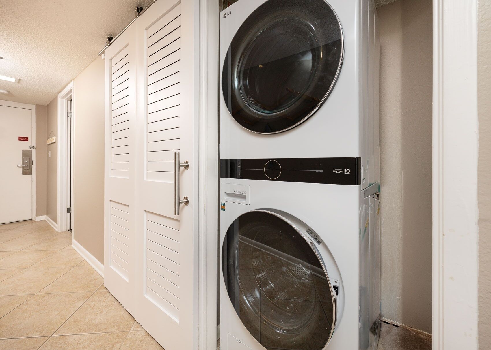 A laundry room with two stacked front-loading washing machines, a door with a handle, and a tiled floor.