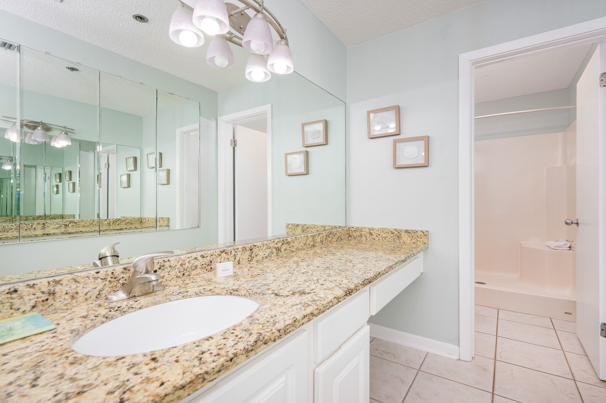 A bathroom with a granite countertop, a white sink, a large mirror, and a shower area.