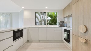 A modern kitchen with white cabinetry, a built-in oven, and a window with a view of palm trees.