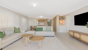 A modern living room with a sofa, two wooden side tables, and a TV on the wall.