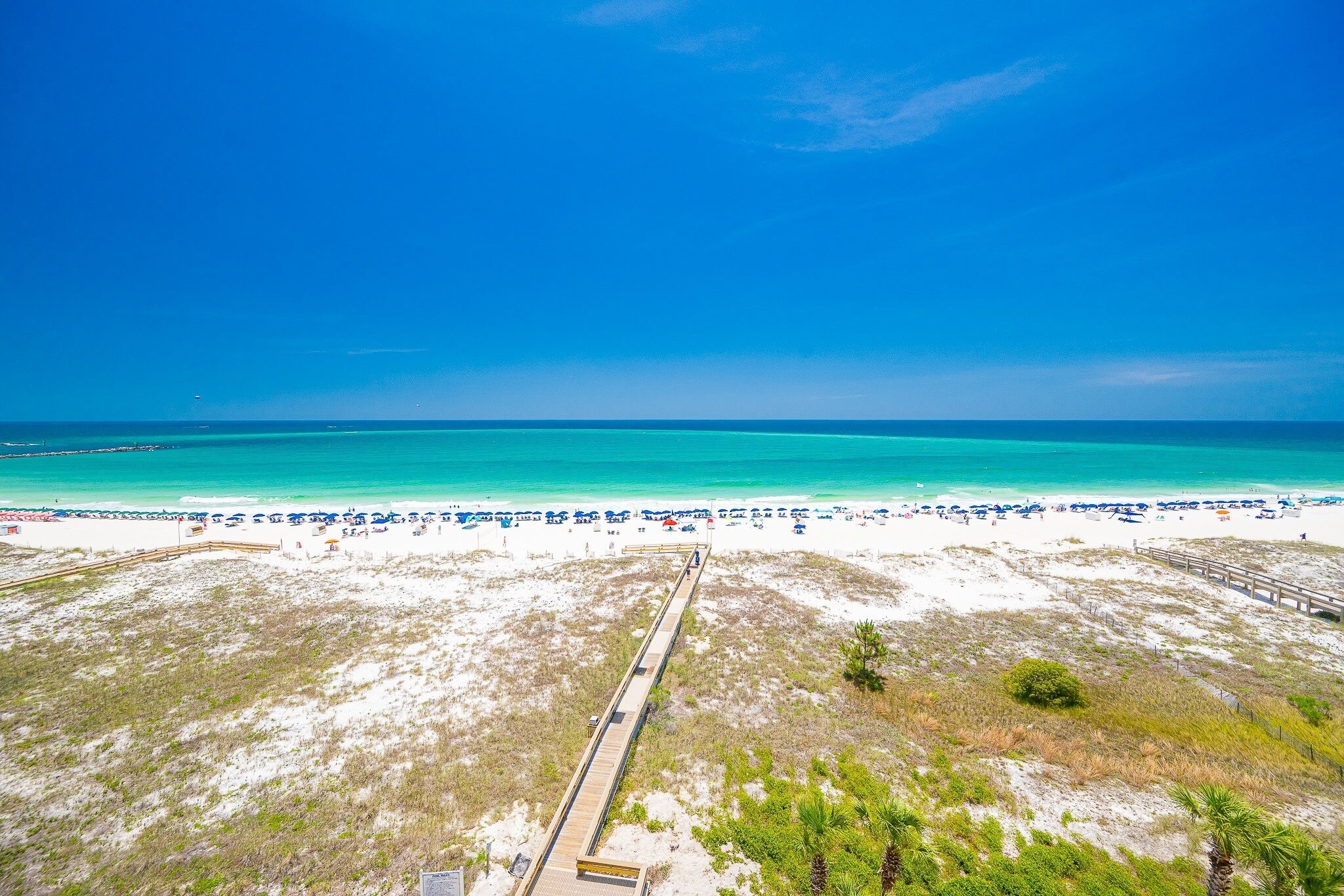A beach with a wooden boardwalk leading to the water, white sand, and clear blue sky.
