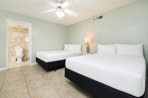 Une chambre d’hôtel avec deux lits, un ventilateur de plafond, une salle de bain avec des toilettes et une douche, et une table de chevet avec une lampe.