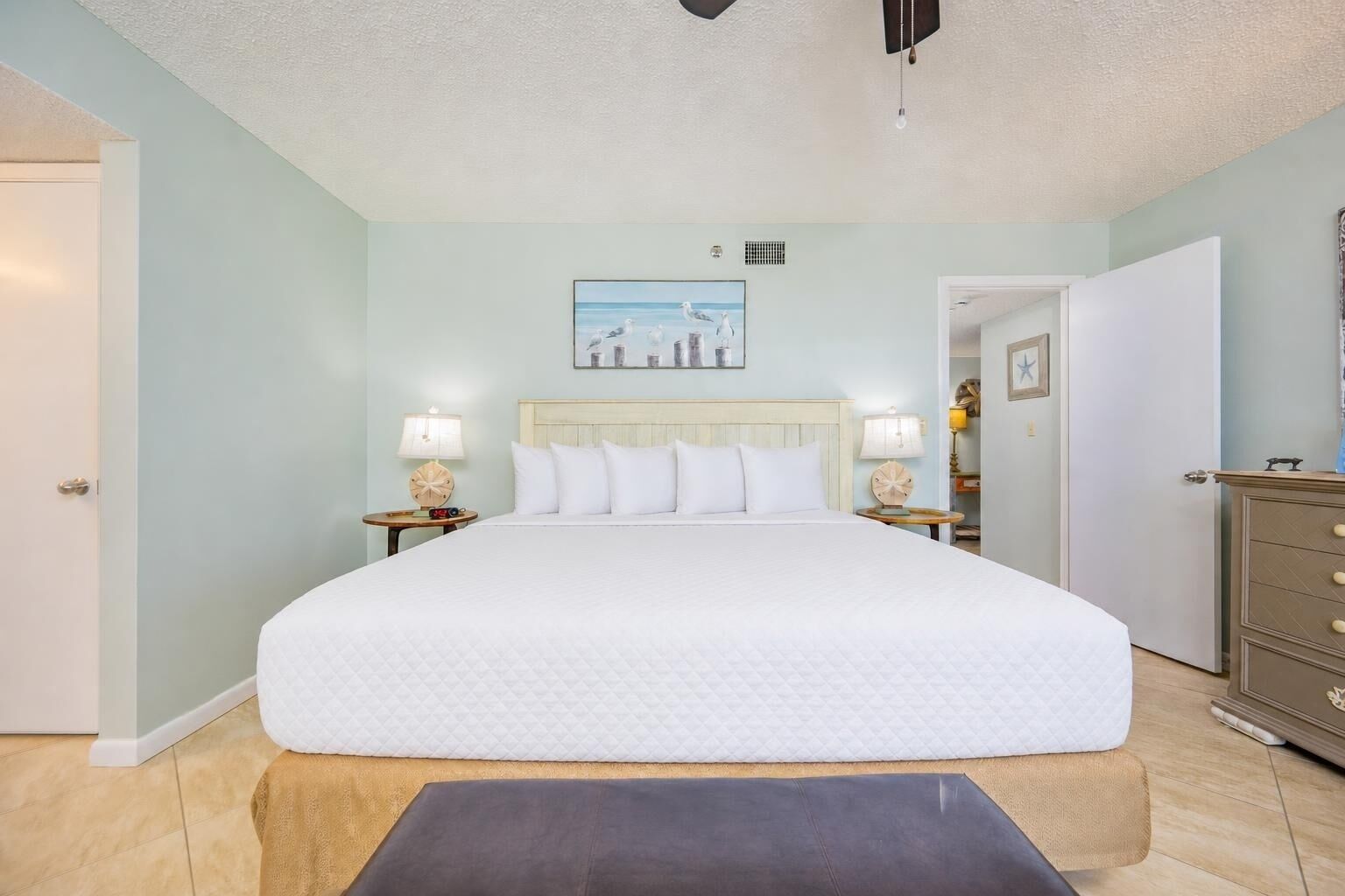A bedroom with a large bed, two bedside tables with lamps, a dresser, and a painting on the wall.