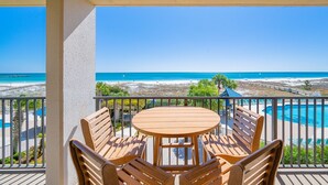 A wooden table and chairs on a balcony with a view of a beach and a pool.