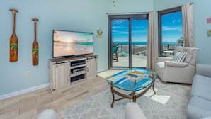 Ein Wohnzimmer mit Fernseher, Holzmöbeln, einem Glastisch und einem Balkon mit Aussicht.