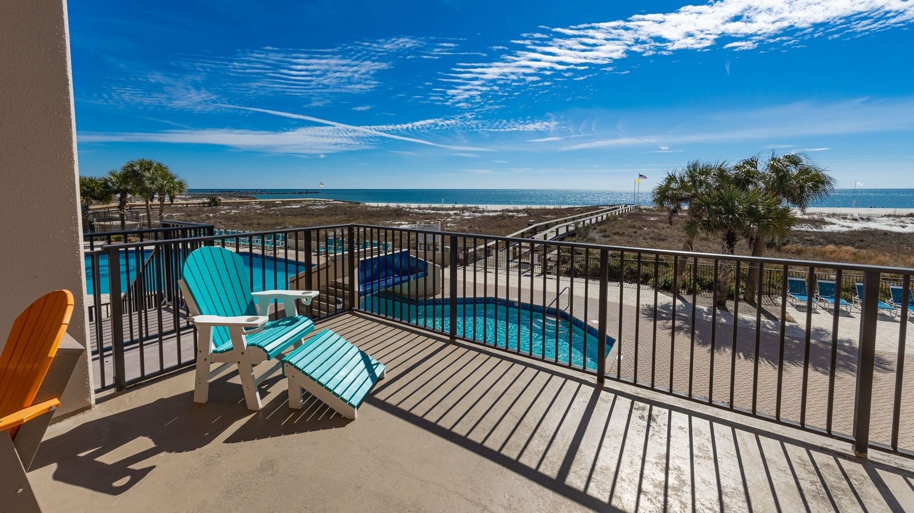 A balcony with a view of the ocean, a pool, and beach chairs.