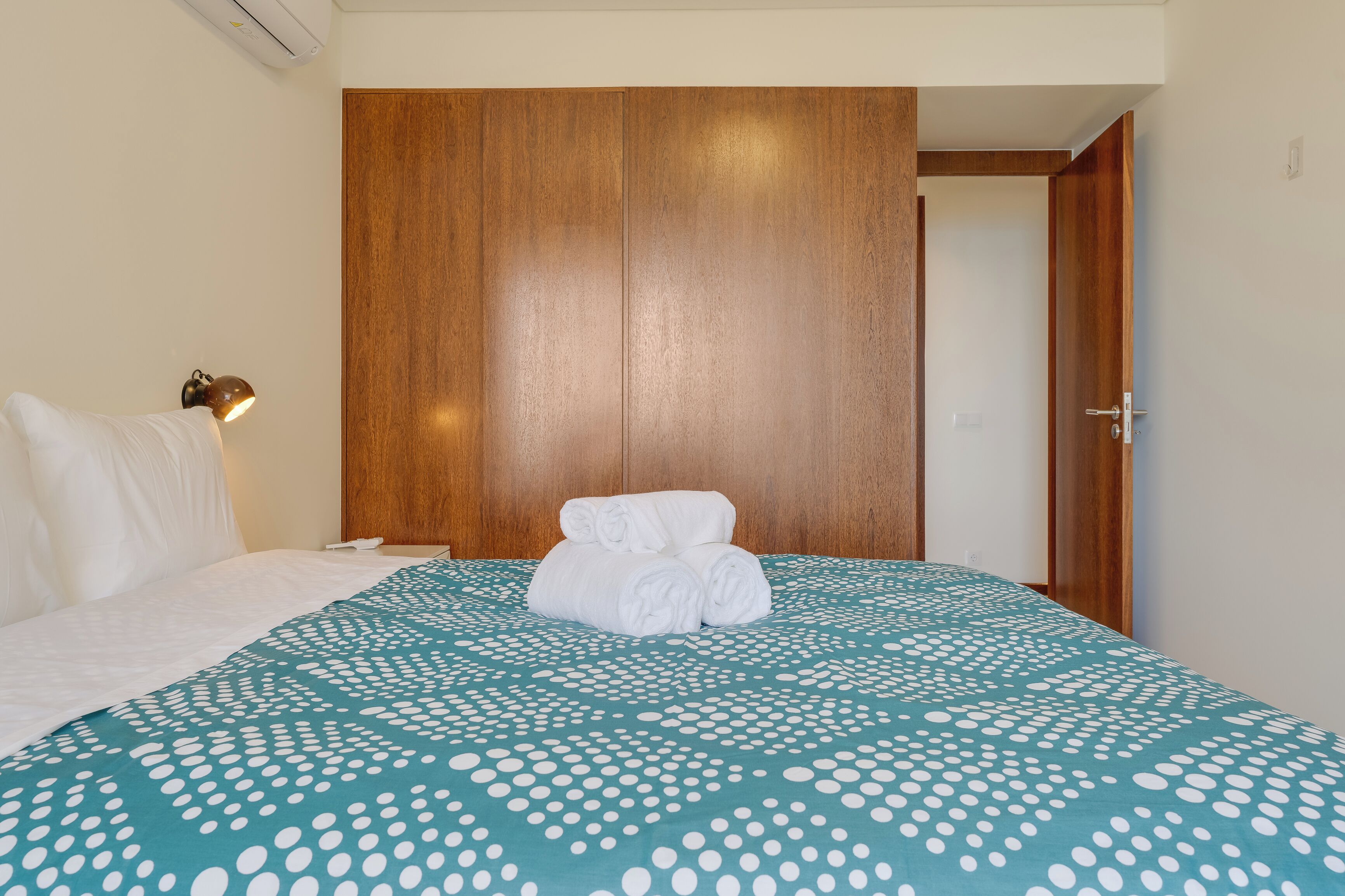 Una habitación de hotel con una cama, un armario de madera y una mesita de noche con una lámpara.