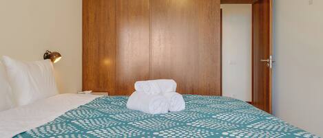 Una habitación de hotel con una cama, un armario de madera y una mesita de noche con una lámpara.