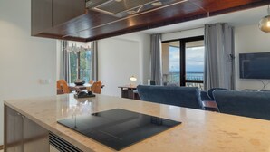 A modern kitchen with a large island, a dining area with a table and chairs, a living room with a sofa, and a balcony with a view. - Carlos Apartment (Funchal)