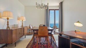 A modern dining area with a wooden table, two lamps, a chandelier, and a view of the sea through large windows. - Carlos Apartment (Funchal)