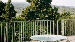 Een metalen tafel en stoelen op een balkon met uitzicht op bomen en heuvels.