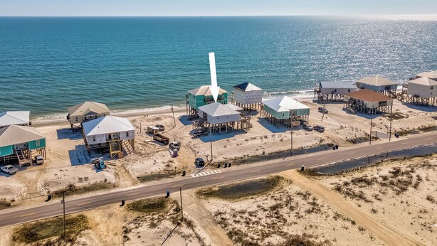 Vista aérea de una zona costera con varias edificaciones sobre pilotes, una carretera y una playa.