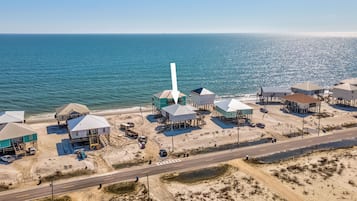 Vue aérienne d’une zone côtière avec de nombreux bâtiments construits sur pilotis, une route et une plage.