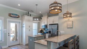 Una cocina moderna con armarios blancos, encimeras de granito, electrodomésticos de acero inoxidable e iluminación colgante.