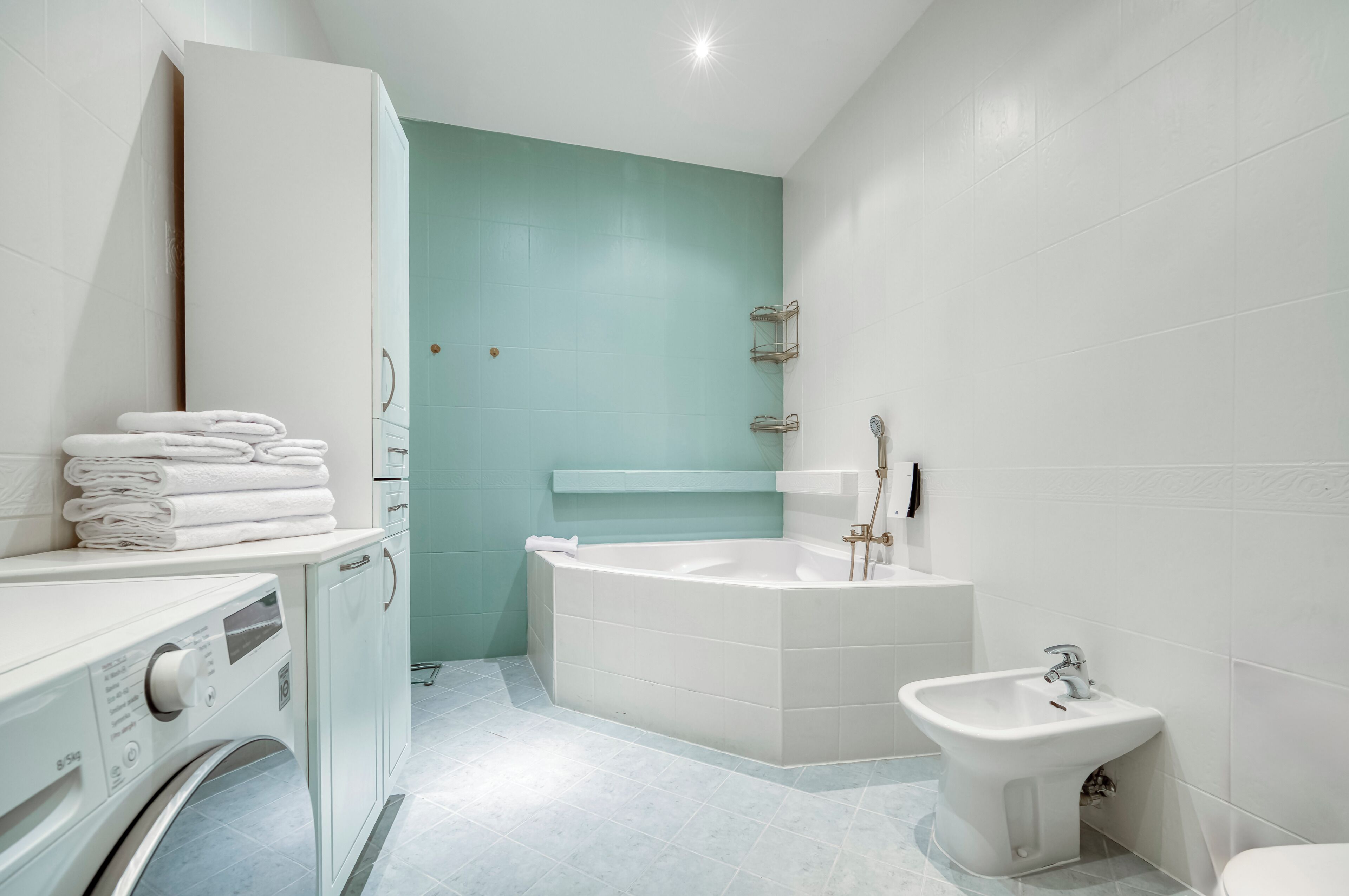 A modern bathroom with a white sink, a freestanding bathtub, a bidet, and a washing machine.