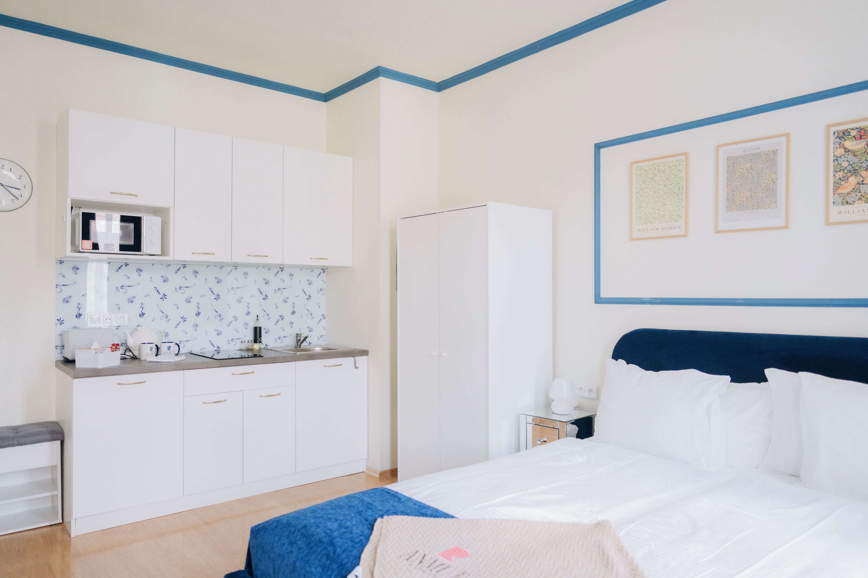 A bedroom with a bed, a nightstand, a dresser, a microwave, and a clock on the wall.