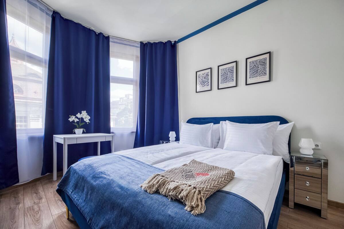 A hotel room with a bed, a bedside table, a lamp, and a nightstand. There are three framed pictures on the wall.
