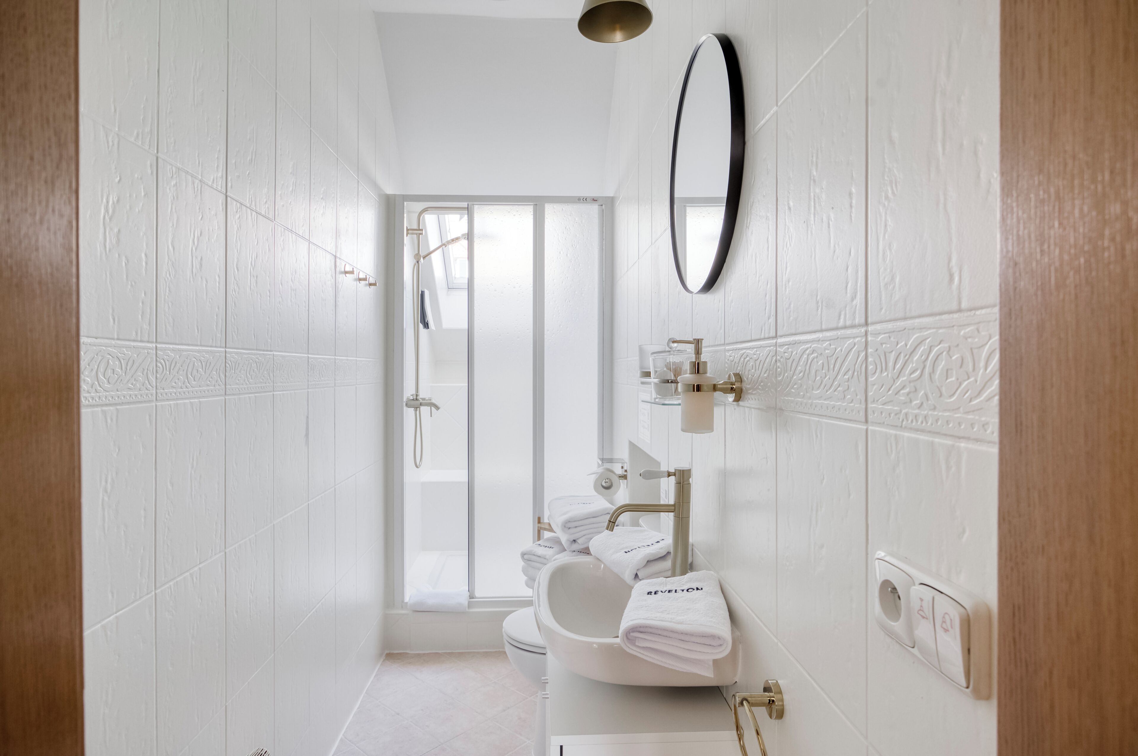 A modern bathroom with a shower, toilet, and sink, featuring white tiles and a large mirror.