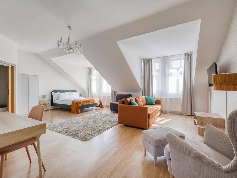 A modern loft-style room with a high ceiling, a dining area, a sofa set, a bed, and a large window.