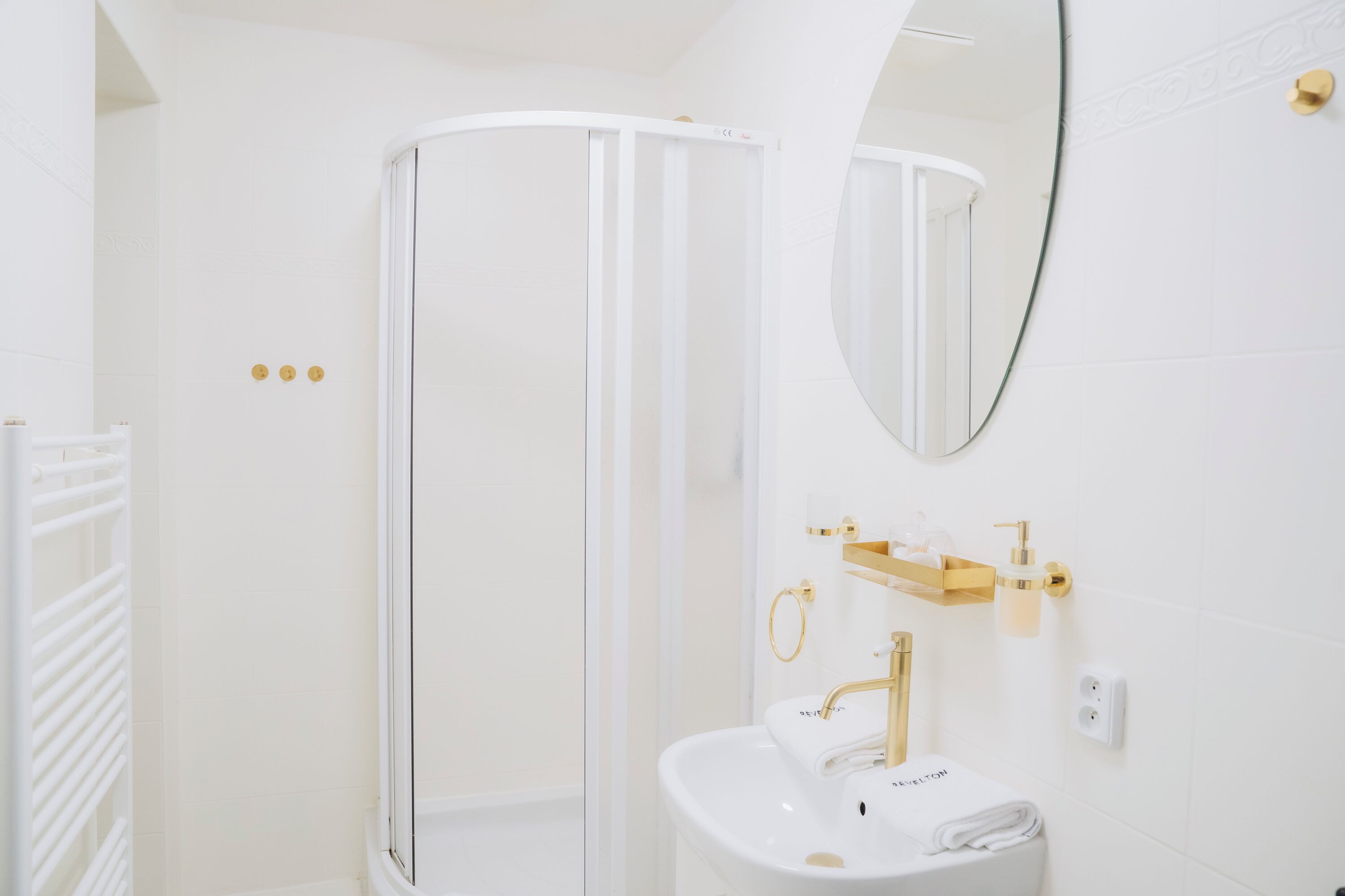 A bathroom with a white shower enclosure, a sink with gold fixtures, and a mirror.