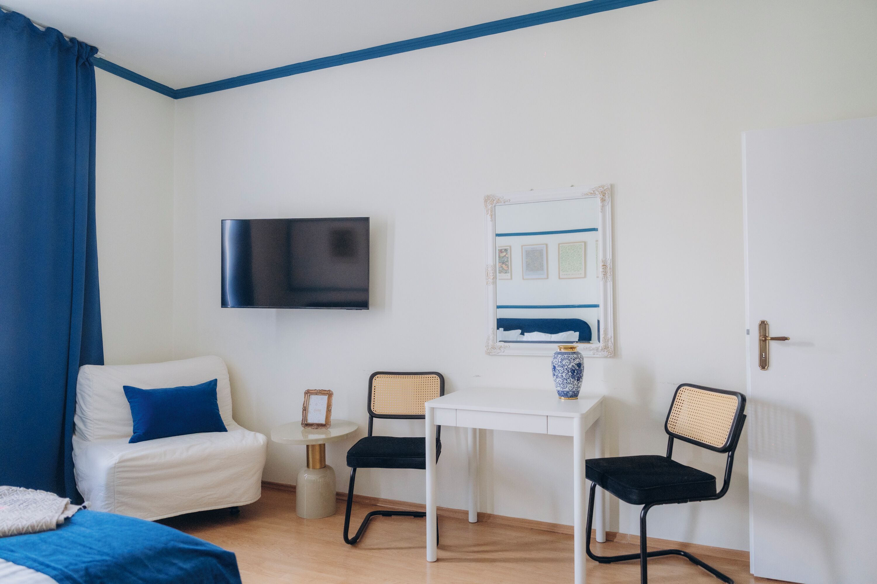 Una habitación con una cama, un escritorio, dos sillas, un televisor y una puerta.
