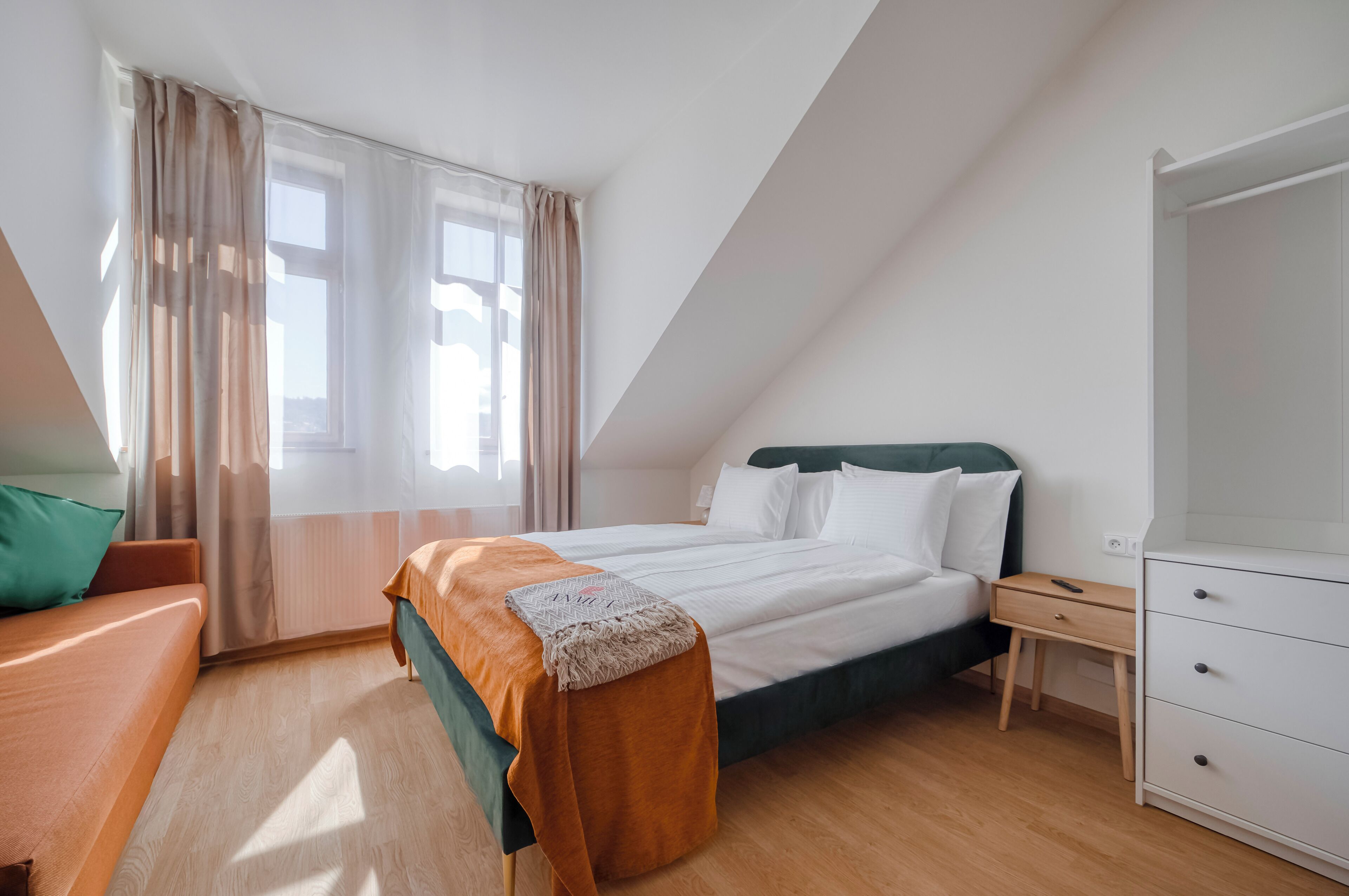 Ein Schlafzimmer mit Bett, Nachttisch, Kommode und einem Fenster mit Vorhängen.