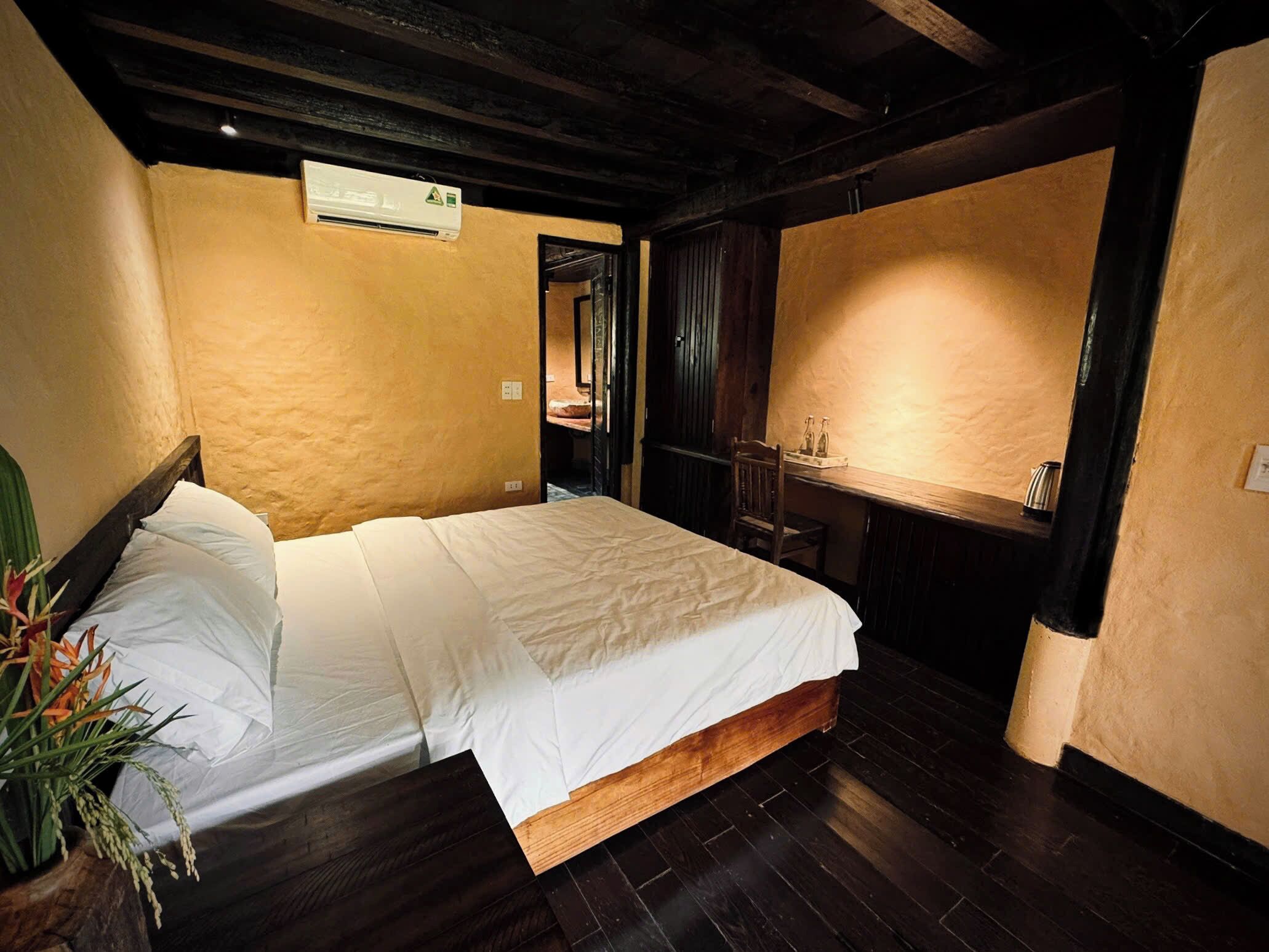 A room with a bed, a small table, and a chair. There is a wooden floor and a ceiling with exposed beams.