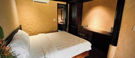 A room with a bed, a small table, and a chair. There is a wooden floor and a ceiling with exposed beams.