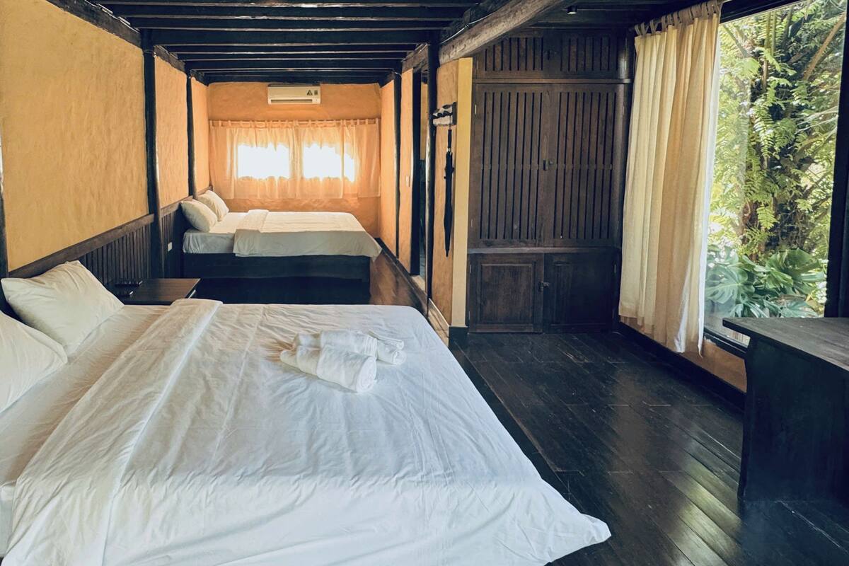 A room with two beds, wooden flooring, and a window with curtains.