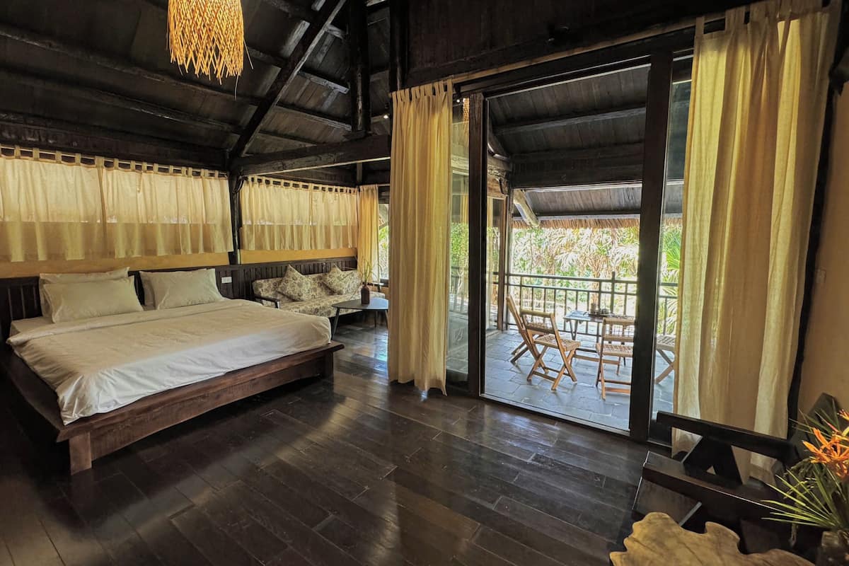 A bedroom with a large bed, wooden flooring, and a sliding glass door leading to an outdoor area with a table and chairs.