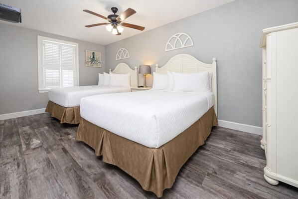 A bedroom with two beds, a ceiling fan, a window with shutters, and a cabinet.