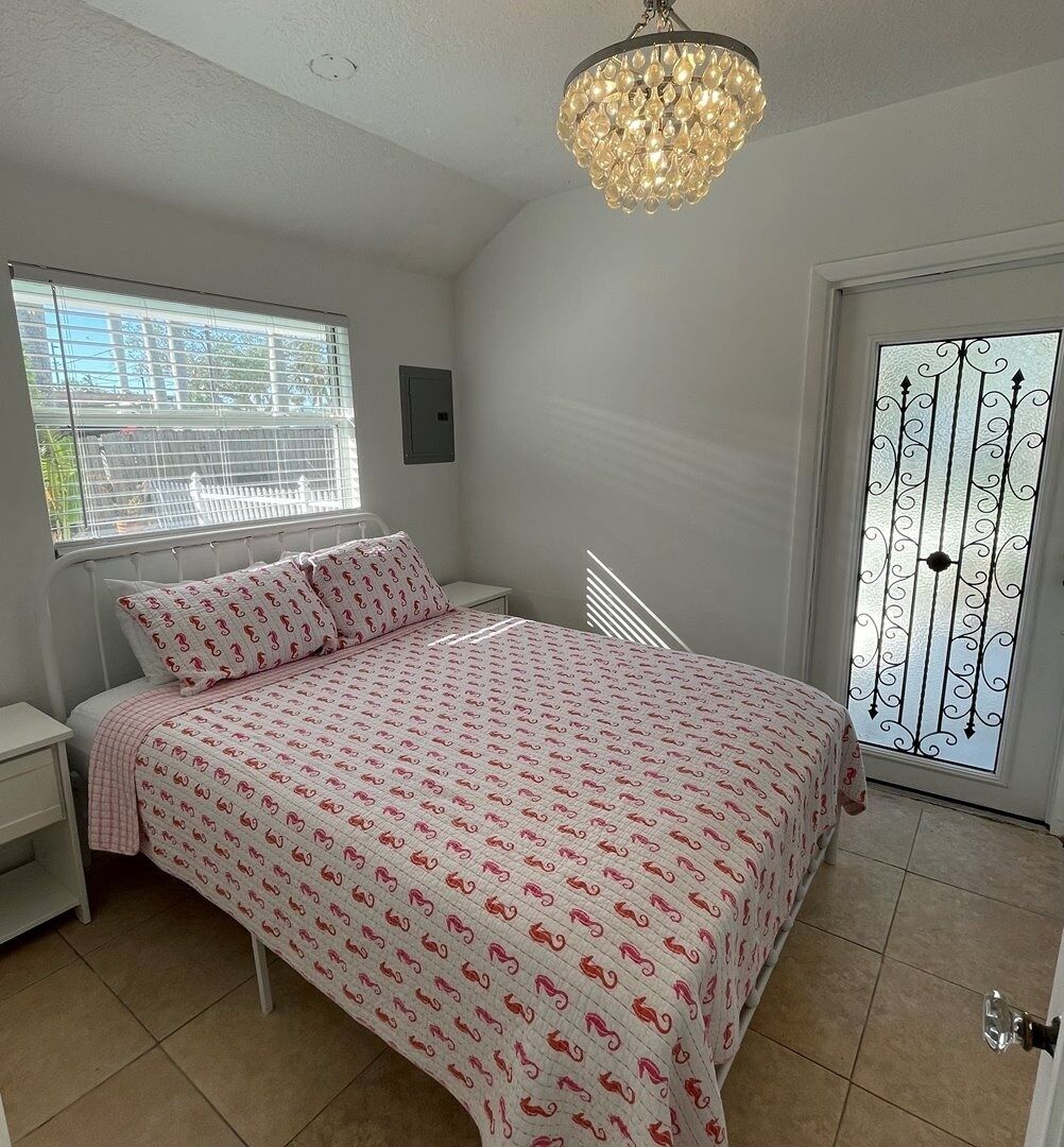 Une chambre à coucher comprenant un lit, une table de chevet, une fenêtre et une porte ornée d’un panneau de verre décoratif.