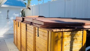 Tinaco de madera al aire libre con techo, rodeado por una terraza de madera y una cerca blanca.