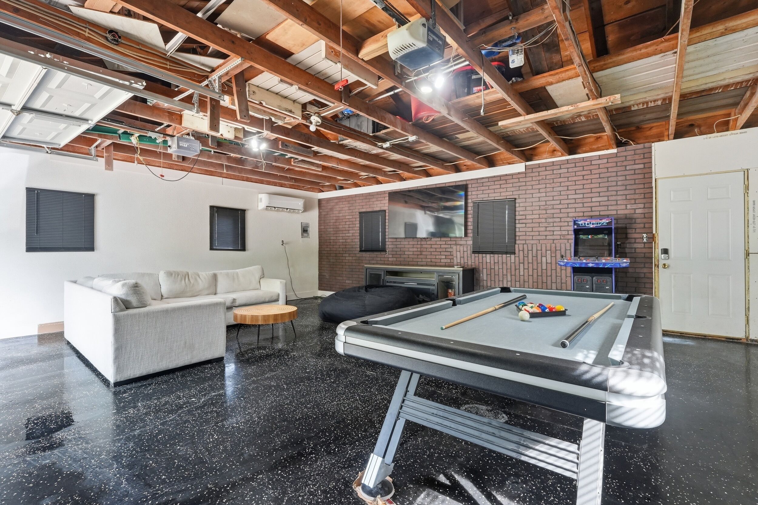 Une pièce avec une table de billard, un canapé, un fauteuil poire, une télévision et un mur en briques.