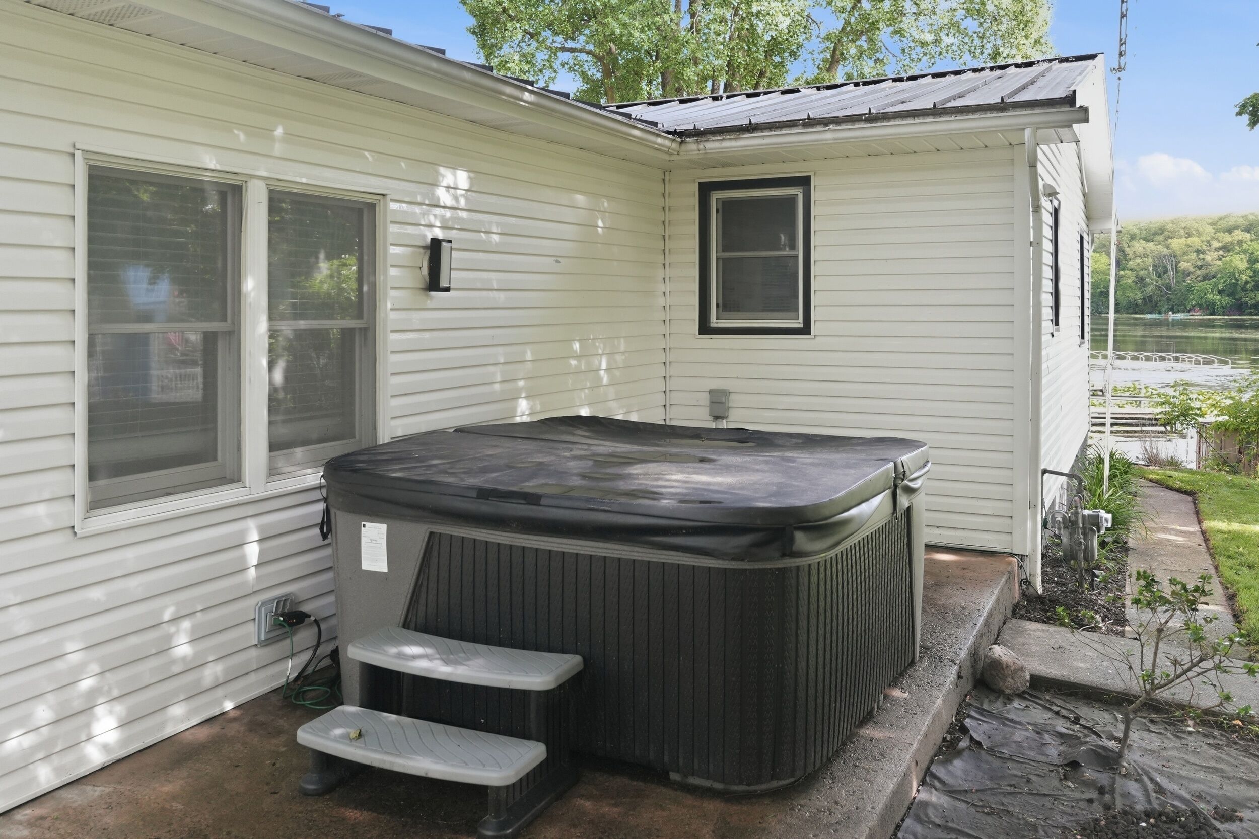 A hot tub with steps, a window, and a door, adjacent to a house with a view of a lake.