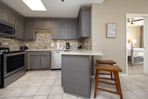 Kitchen features a central island with stools, appliances, and a backsplash with small, rectangular tiles.