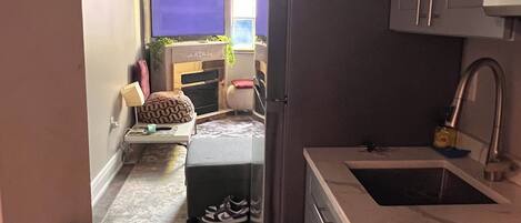 Cocina estrecha con estufa, lavamanos y armarios. Un televisor está montado en la pared en la habitación contigua.