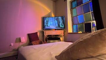 A hotel room with a bed, a television, a window with a view of the night sky, and a ceiling fan.