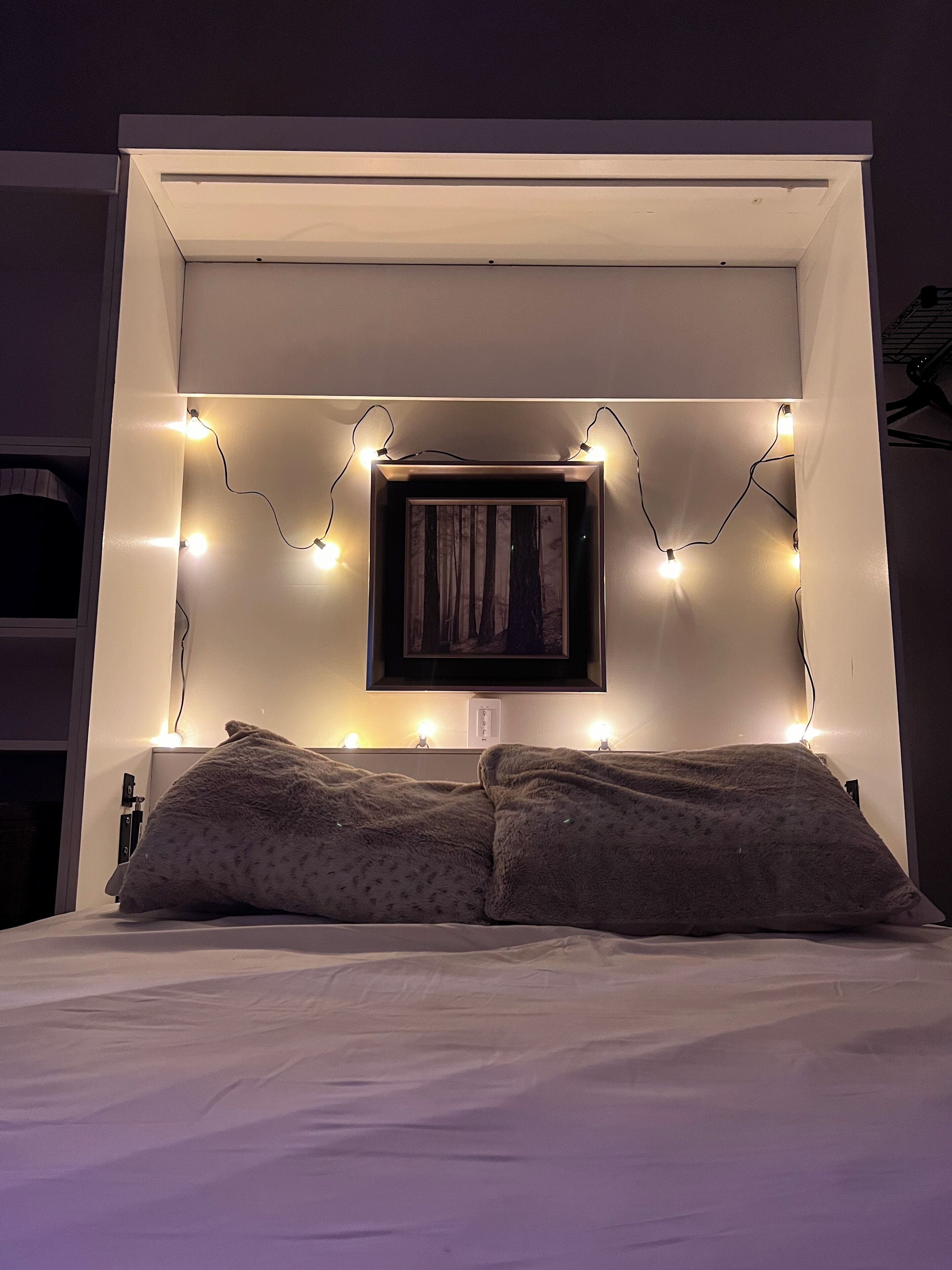 Una cama con cabecera, dos almohadas y luces de cadena.