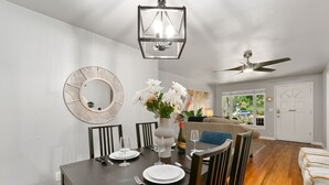 A dining area with a dark wooden table, white plates, and a vase with flowers. There is a ceiling fan and a large mirror on the wall. - Urban Nest | Garage, Sunroom & Fenced Yard (Fort Collins)