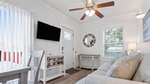 Ein Wohnzimmer mit einer Couch, einem an der Wand befestigten Fernseher, einem Deckenventilator und einem Fenster mit Jalousien.