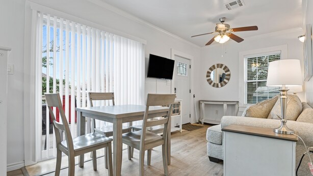 Ein modernes Wohnzimmer mit Essbereich, Deckenventilator, Flachbildfernseher und einer Couch mit Lampe.