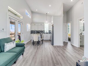 Et moderne køkken med hvide skabe, et spiseområde med et bord og stole, samt en grøn sofa.